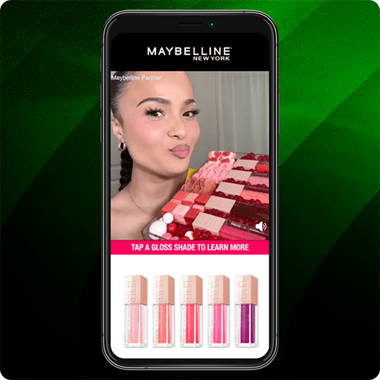 Smartphone mit einer interaktiven Maybelline-New-York-Werbung, fünf Lipgloss-Farbtönen und der Aufforderung „Tap a gloss shade to learn more“ vor einem grün gestreiften Hintergrund.