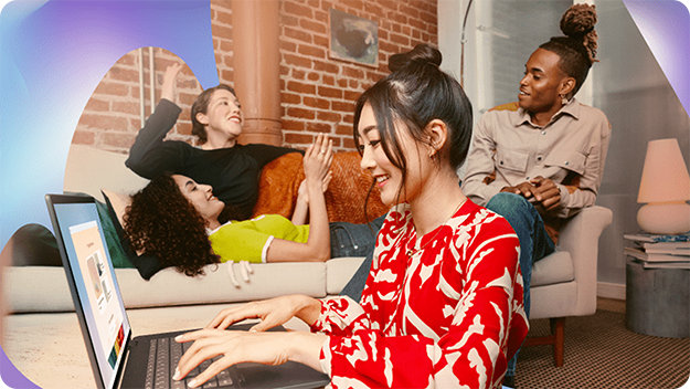 A person working on a laptop while others relax on a couch in a modern living room with exposed brick walls and colorful decor.