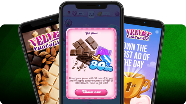 Drei Smartphones vor grünem Hintergrund mit Candy-Crush-Belohnungen und Velvet-Chocolate-Werbung.