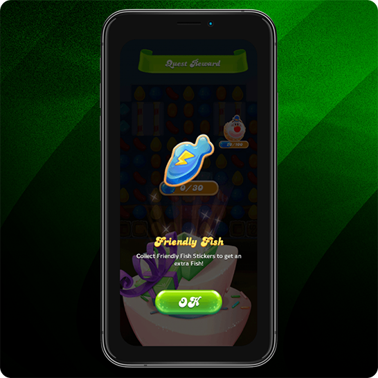 Smartphone mit einem Candy-Spiel und einem Belohnungsbildschirm mit einem blauen „Friendly Fish“-Icon, Hinweisen zum Sammeln von Stickern und einem grünen „OK“-Button vor einem grün gestreiften Hintergrund.