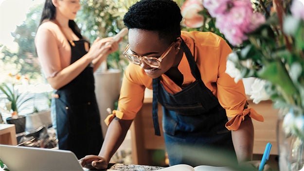 People working in a flower shop using a laptop and mobile device.