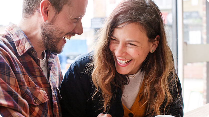 Two people sitting in a coffee shop and laughing.