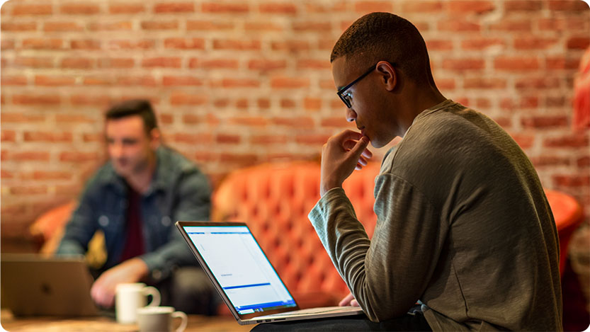 Two people working on laptops in a casual setting with a brick wall background.