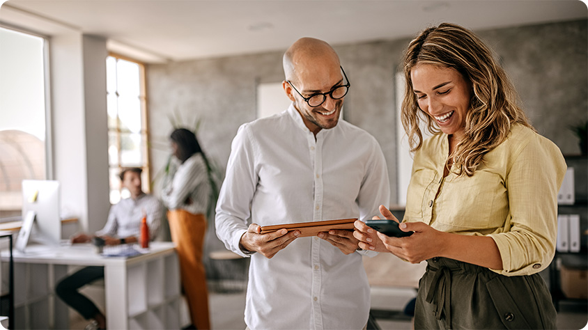 Cheerful female businesswoman standing with colleague looking at a digital tablet in a modern office space